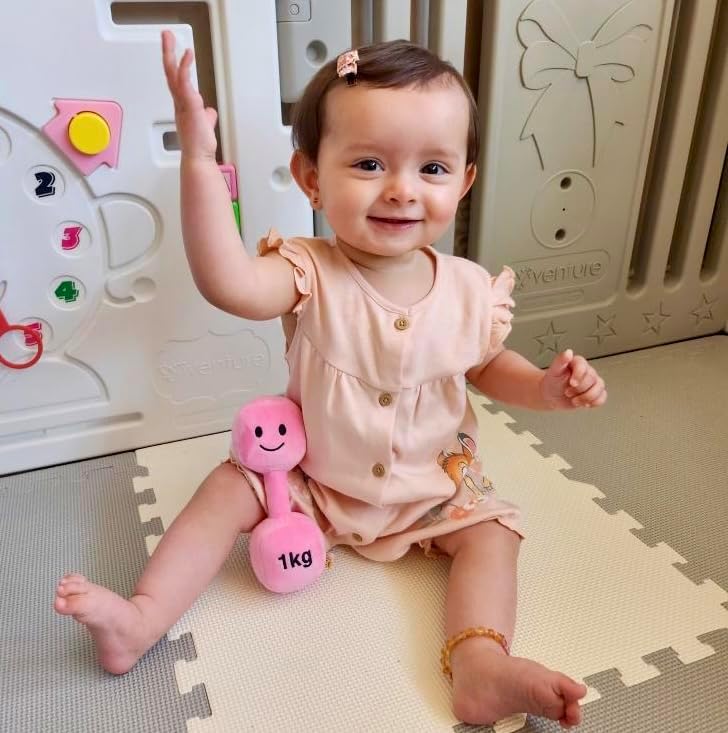 Baby girl smiling while holding a Candy Chateau Pink dumbbell, enjoying joyful playtime with Hazza Toyz fitness-inspired toys for toddlers.