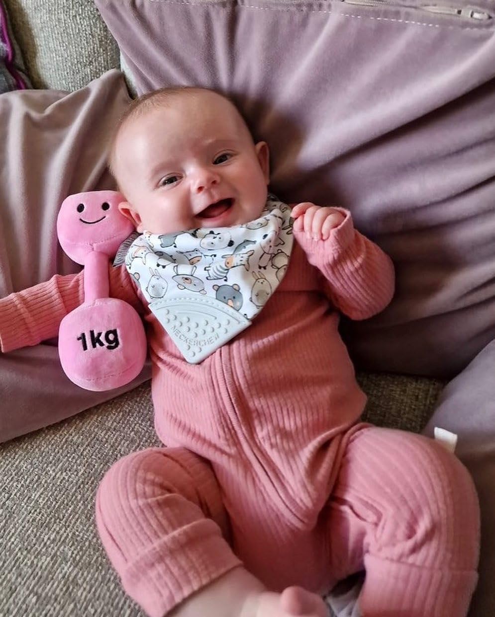 Baby lying down and laughing while holding a Candy Chateau Pink dumbbell, having fun with Hazza Toyz fitness-inspired toys for toddlers.