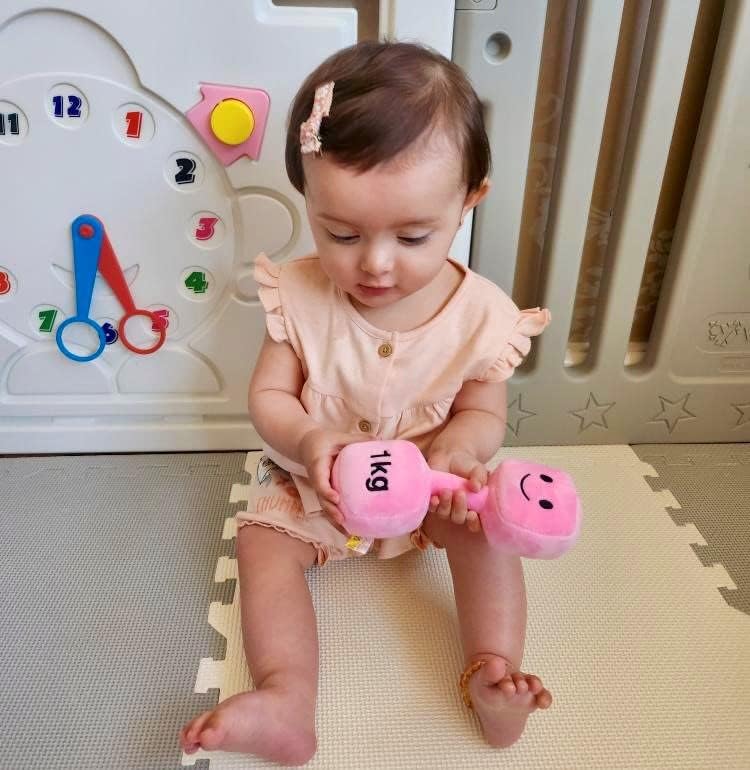 Baby on a playmat holding and intently looking at a Candy Chateau Pink dumbbell, engaging with Hazza Toyz fitness-inspired toys for toddlers.